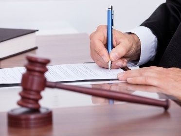 A judge signing a document. There is a gavel on the desk.