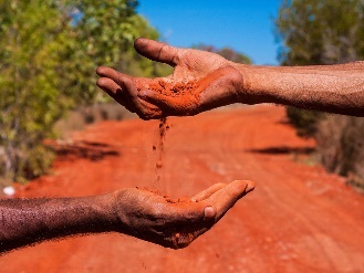2 First Nations peoples holding red dirt in the outback.