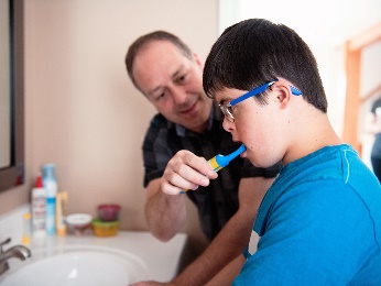 A man is helping a teenager brush their teeth.