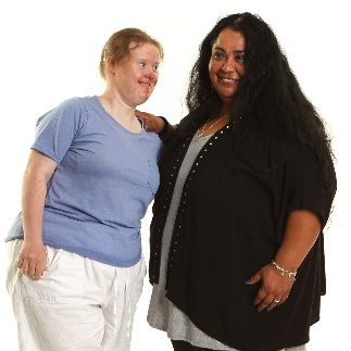 A woman offering support to a person with Down syndrome. They are both smiling.