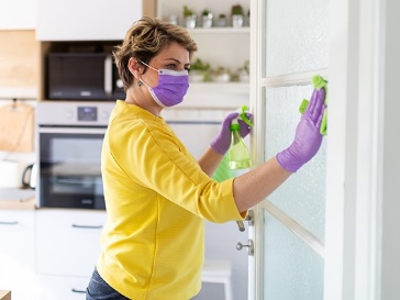 An NDIS worker cleaning a glass door in a kitchen.