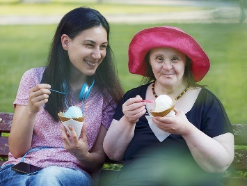 A participant and a support worker smiling and eating ice cream together.
