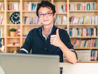 An NDIS worker using a laptop and giving a thumbs up. 