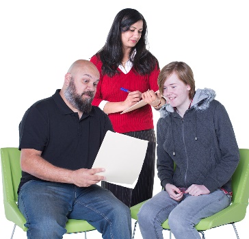 A participant and a worker looking at a document together. Behind them is a supervisor writing notes.