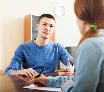 2 people having a conversation. One of them is writing on a document.