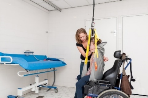 A worker using a hoist to help a participant out of their wheelchair and onto a changing table.