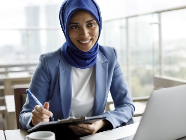 A worker using a laptop and writing on a document.