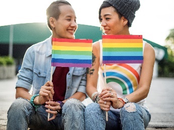 2 people holding rainbow pride flags. 