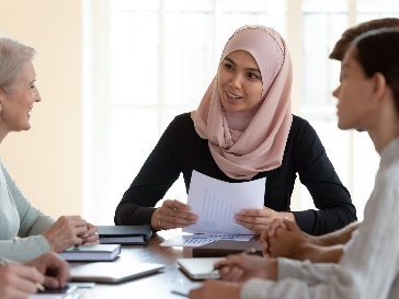 A group of people having a conversation at a desk.