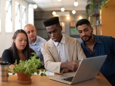 A diverse group of people looking at a laptop together. 